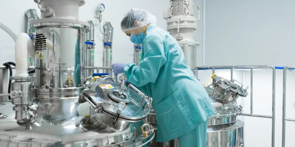 Worker inspecting industrial mixing tanks inside a third-party chemical manufacturing plant.