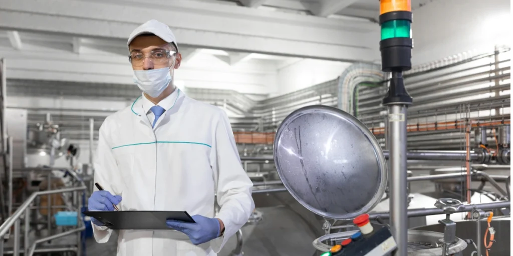 Custom Toll Manufacturing quality control specialist inspecting machinery with clipboard in factory environment